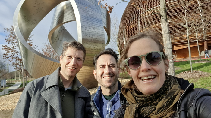 to menn og en kvinne som smiler i sola og står foran Cern